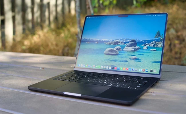 مک&zwnj;بوک پرو M5 باز شده روی میز با صفحه&zwnj;نمایش روشن